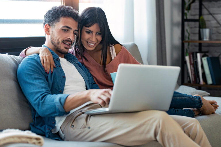 Shot of happy beautiful couple using computer while sitting on the couch at home.